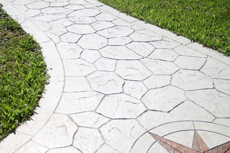 Stamped concrete walkway with a stone-like pattern and decorative compass rose, flanked by green grass.