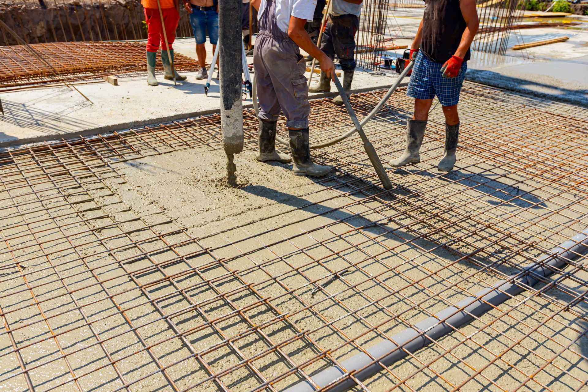 Construction workers pouring concrete onto a steel rebar grid on a building site.