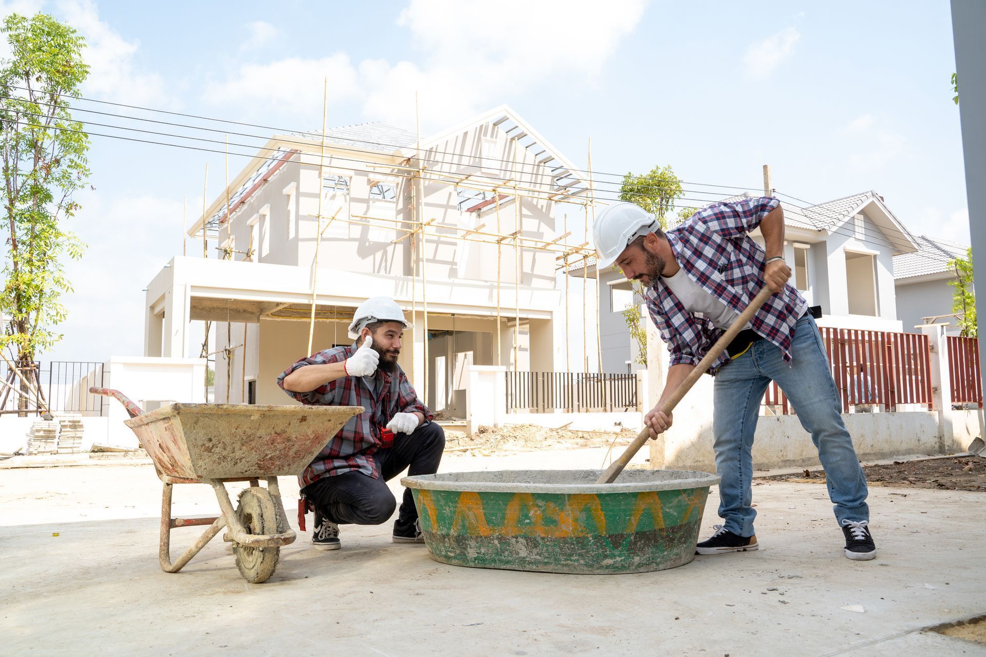 A concrete contractor holds a thumbs up while another is mixing cement at a residential construction site.