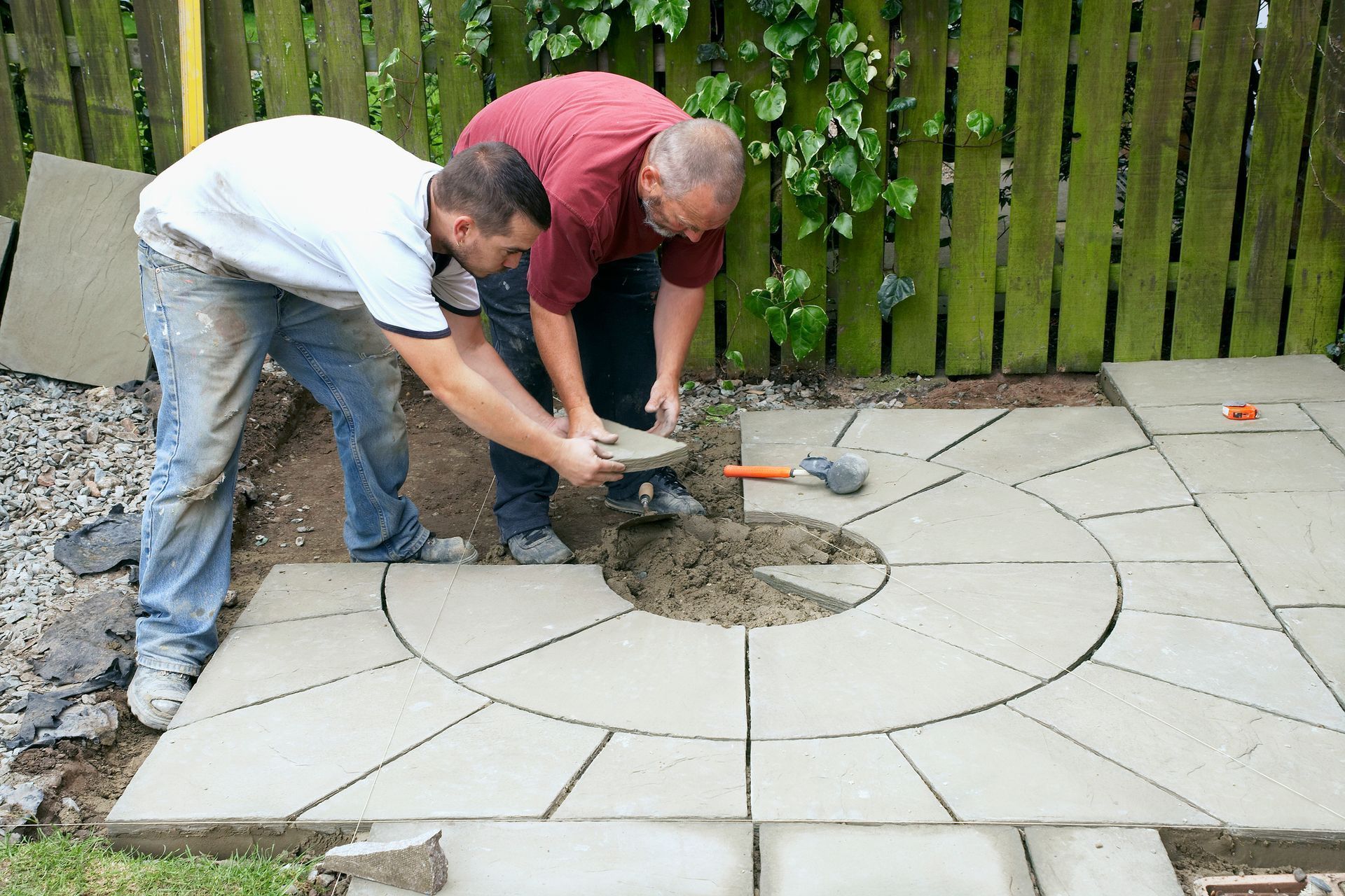 Two men installing circular paving stones in a garden.