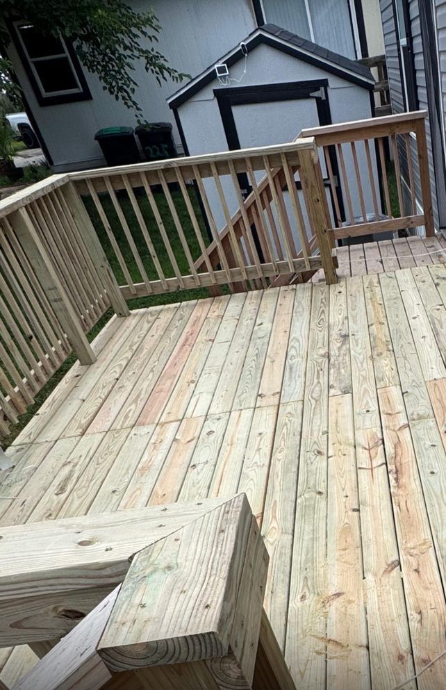 A high-angle view of a new wooden deck with railings, overlooking a backyard with a small shed and greenery.