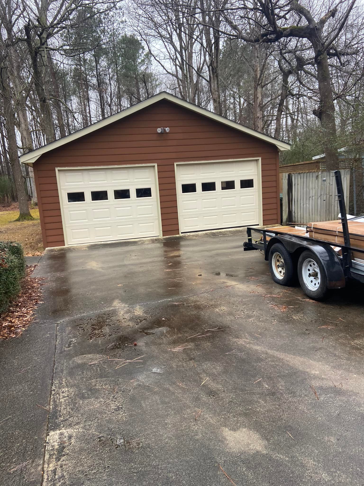 A trailer is parked in front of a garage with two garage doors.