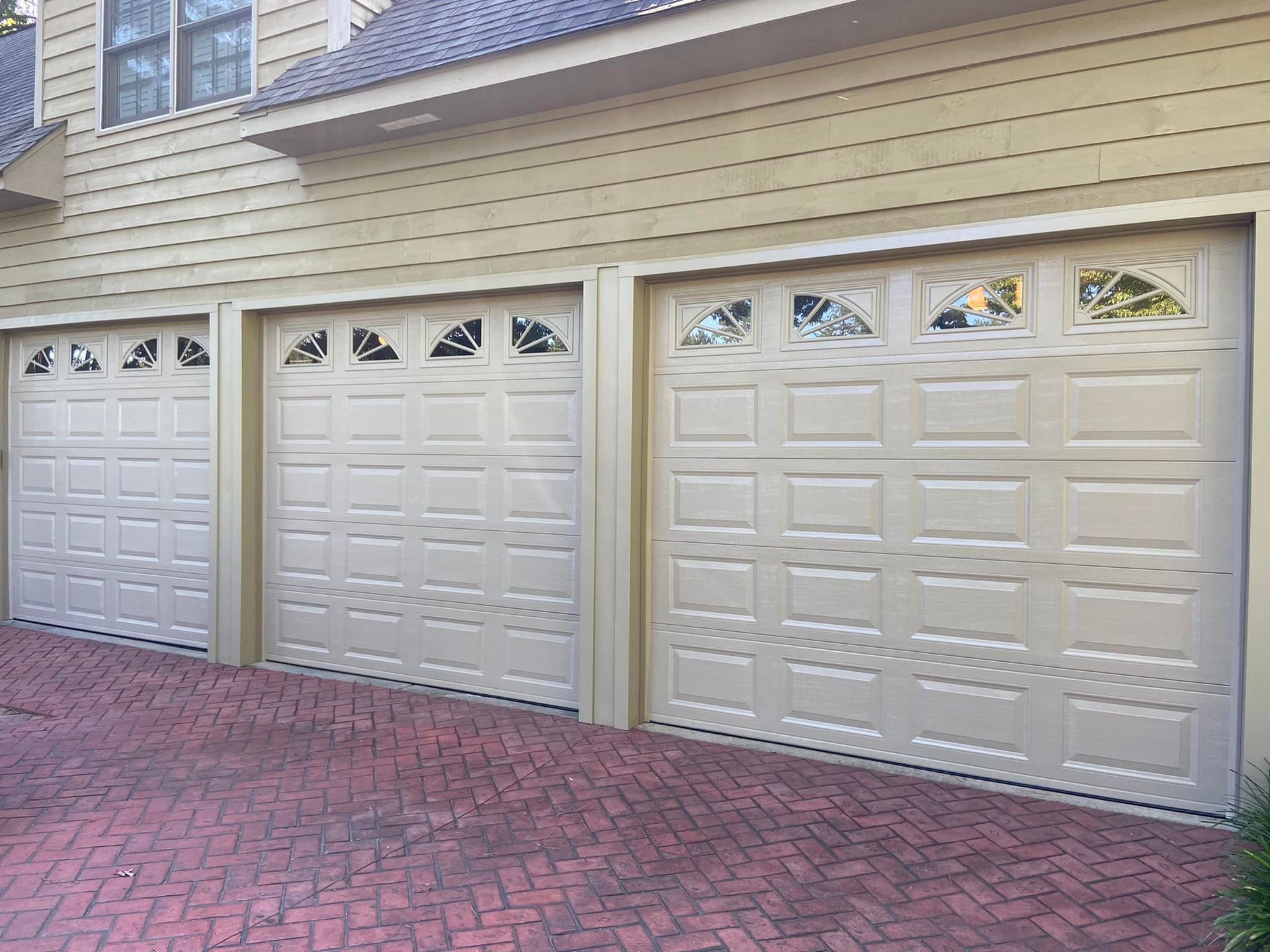 A row of white garage doors on a brick driveway.