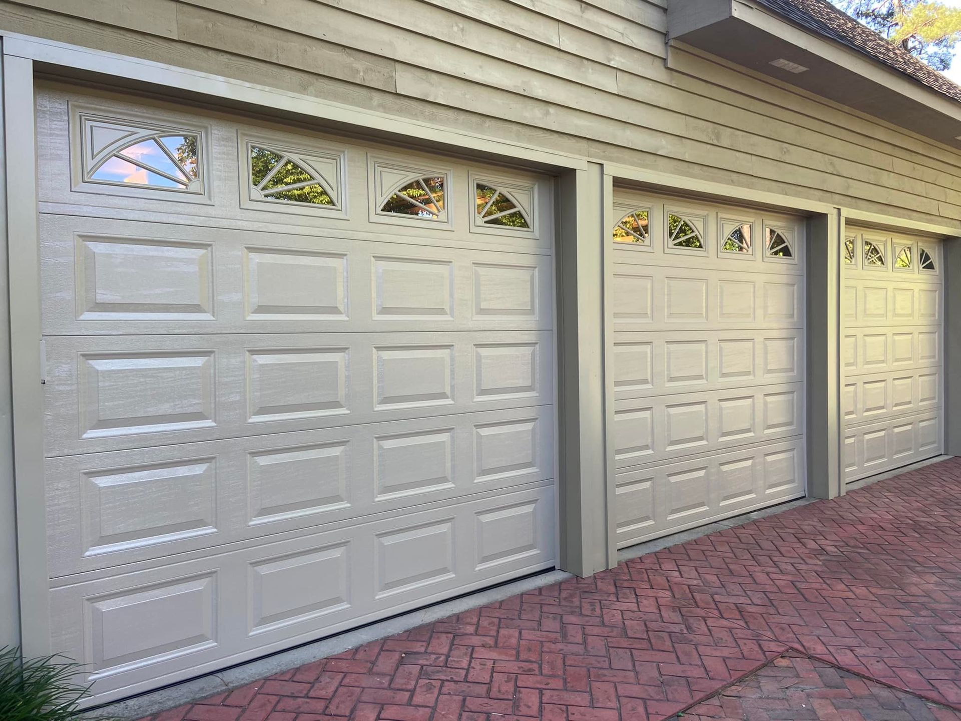 A row of white garage doors on a brick driveway.