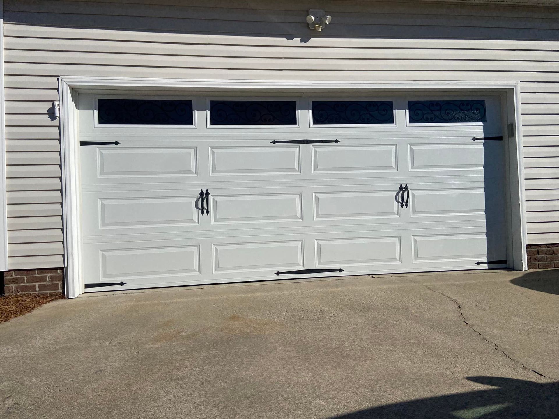 A white garage door is sitting in front of a white house.
