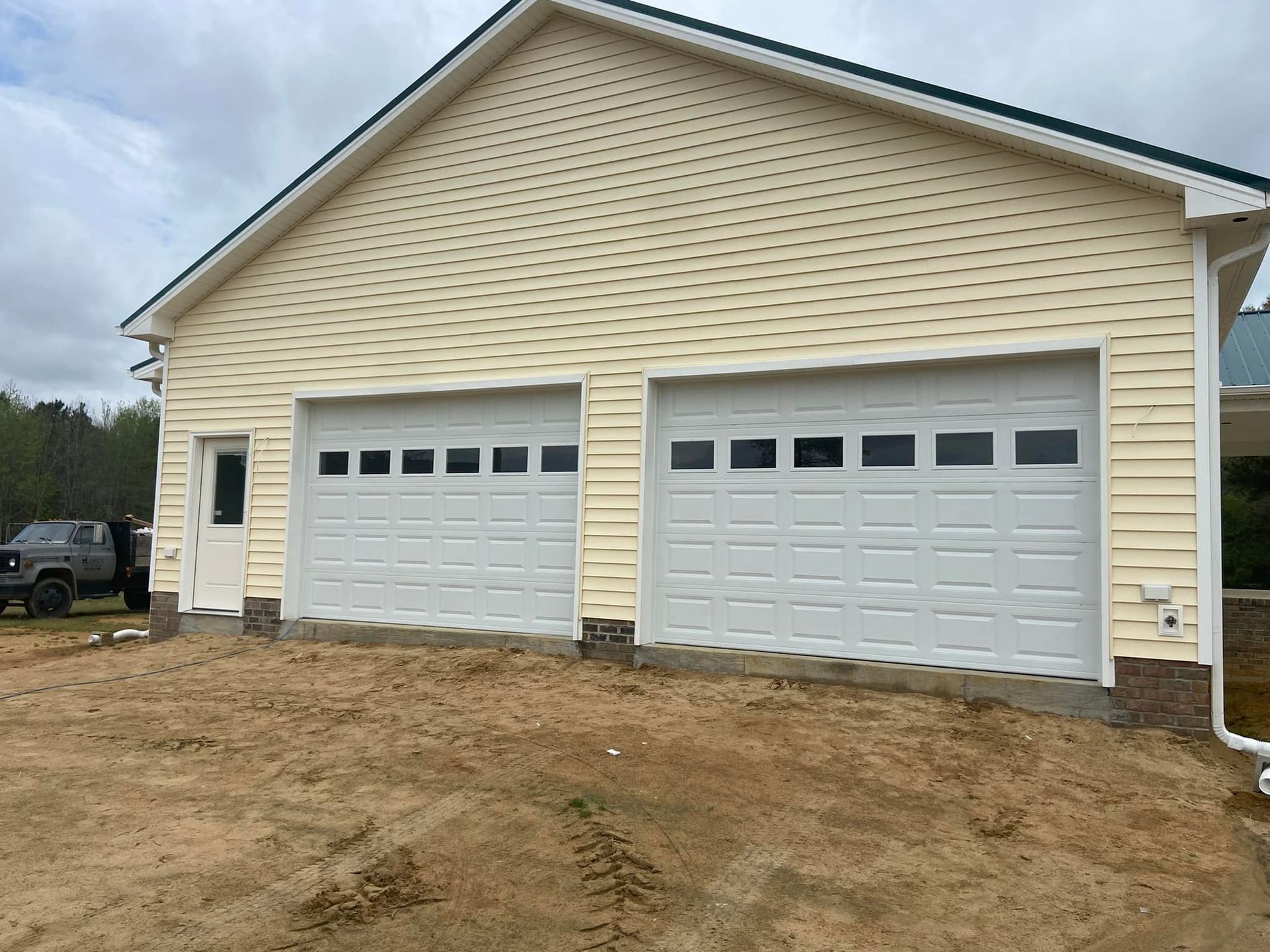 A garage with three white garage doors and a truck parked in front of it.
