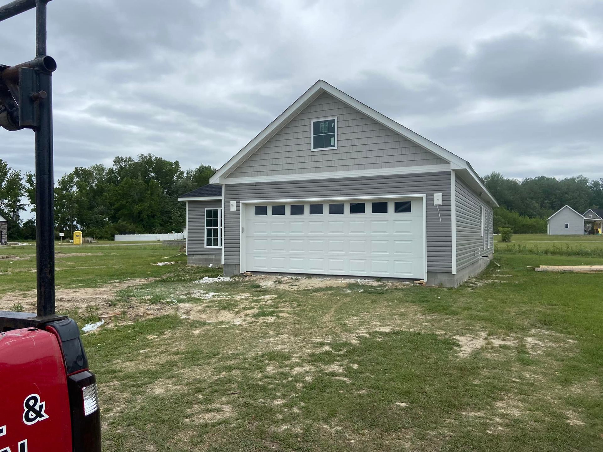 A house with a large garage door is sitting in the middle of a grassy field.