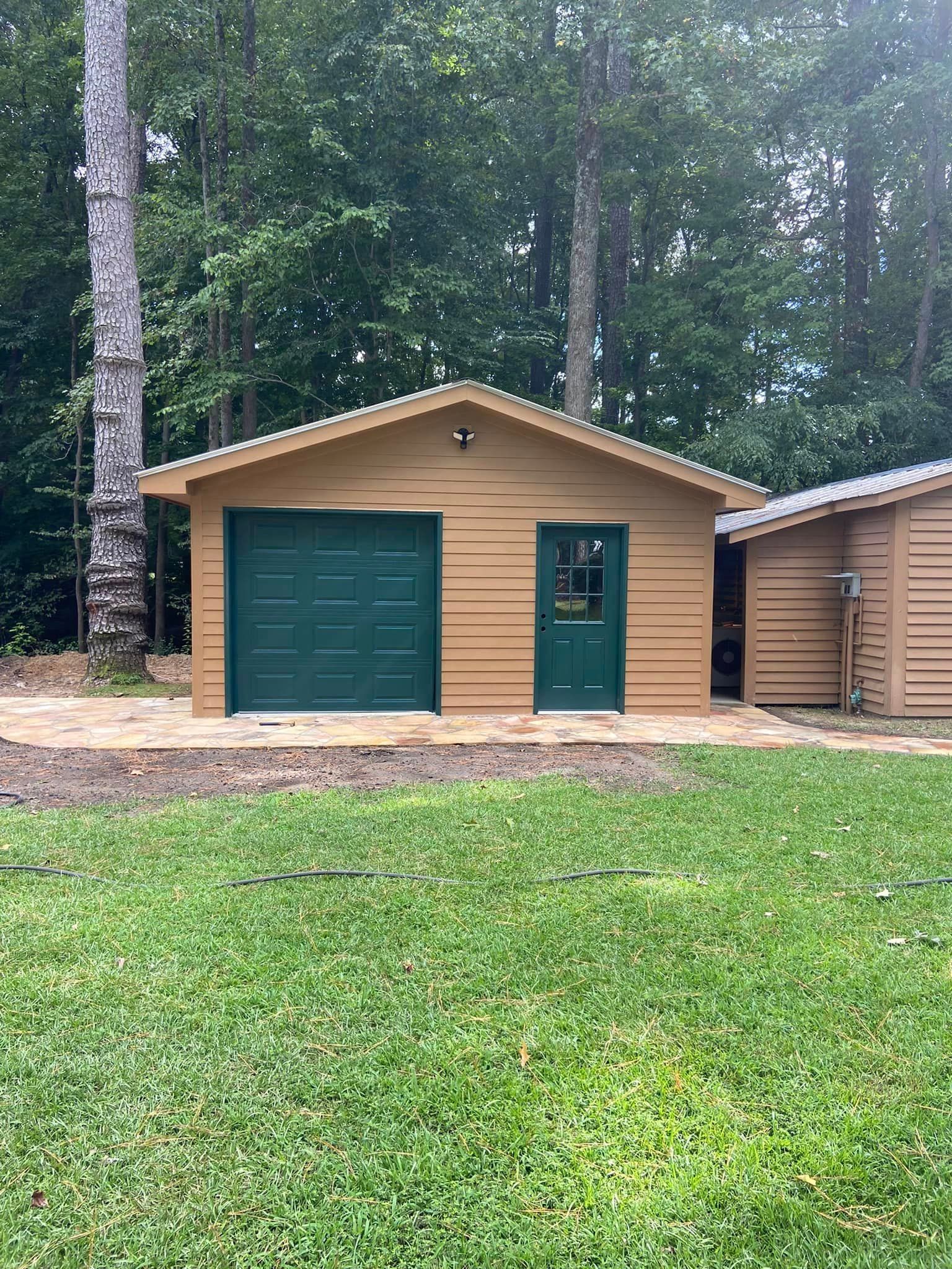A garage with a green door is sitting in the middle of a lush green field.