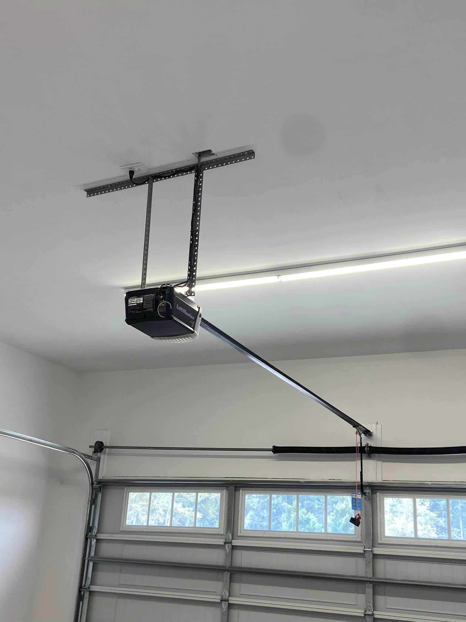 A garage door opener is hanging from the ceiling above a garage door.