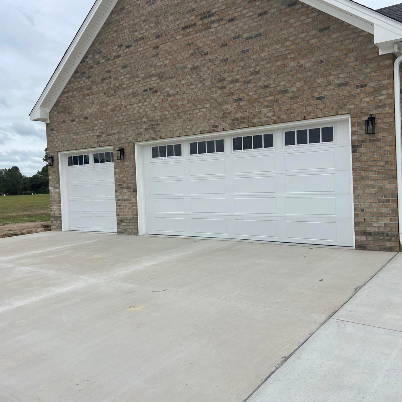 A brick building with two white garage doors and a concrete driveway.