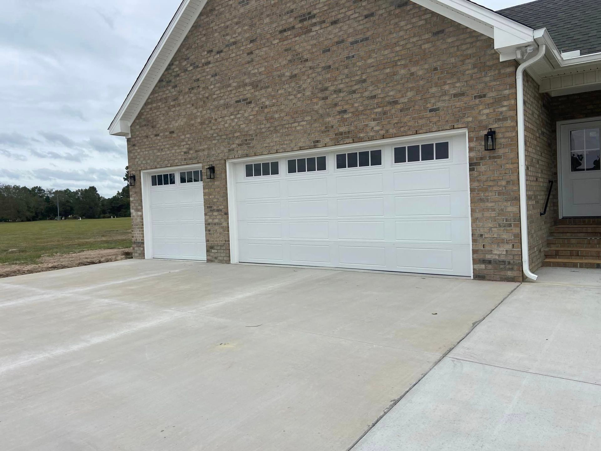 A brick house with two white garage doors and a concrete driveway.