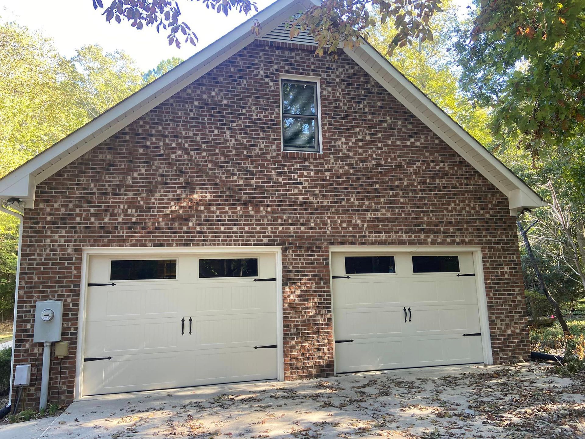 A brick garage with two white garage doors and a window.