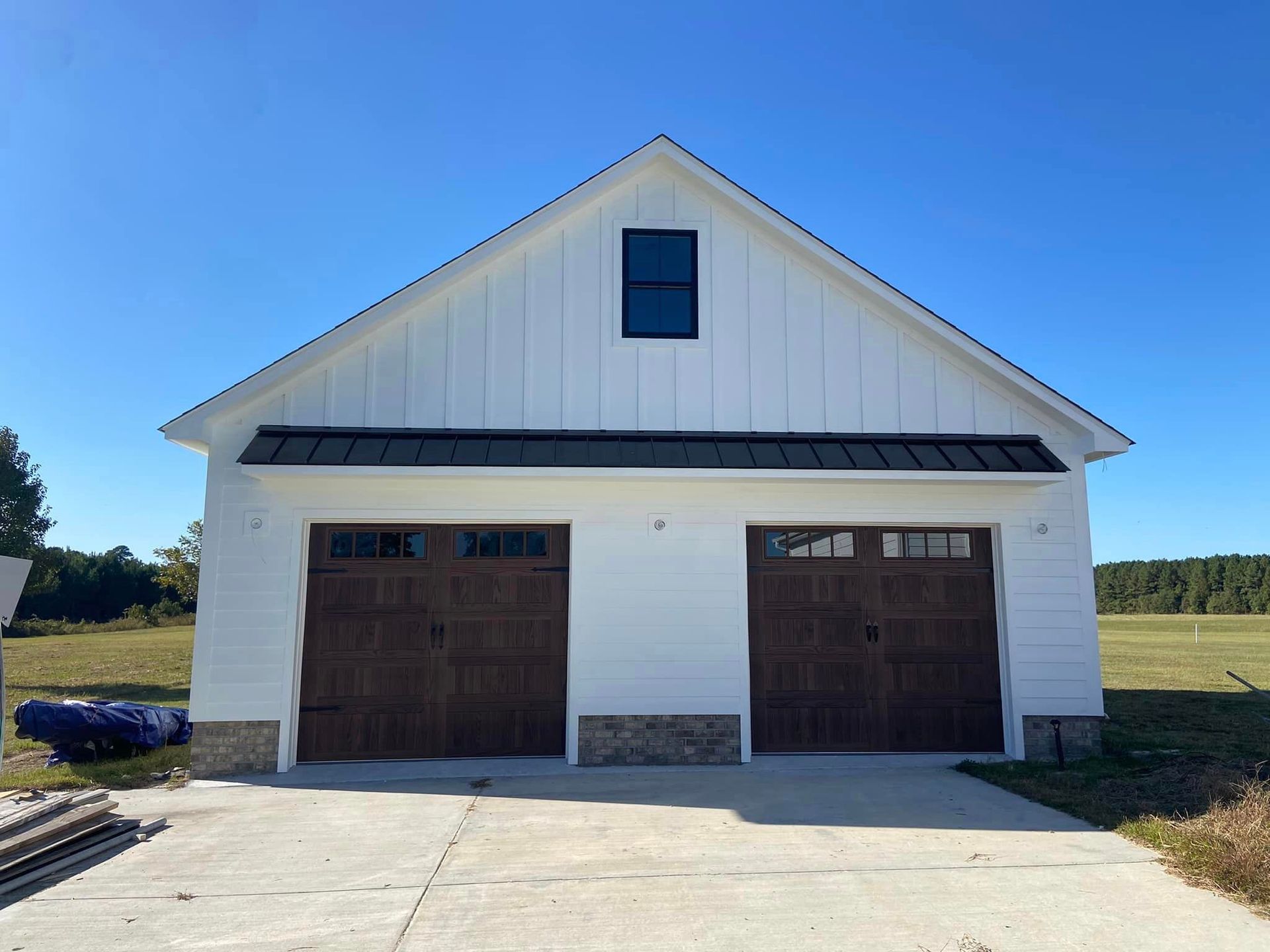 A white garage with brown garage doors and a black roof.