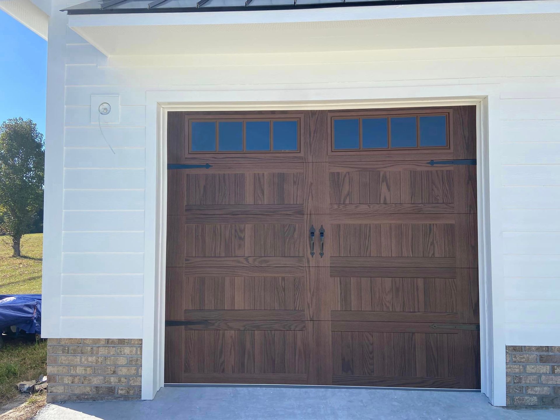 A brown garage door is sitting on the side of a white house.