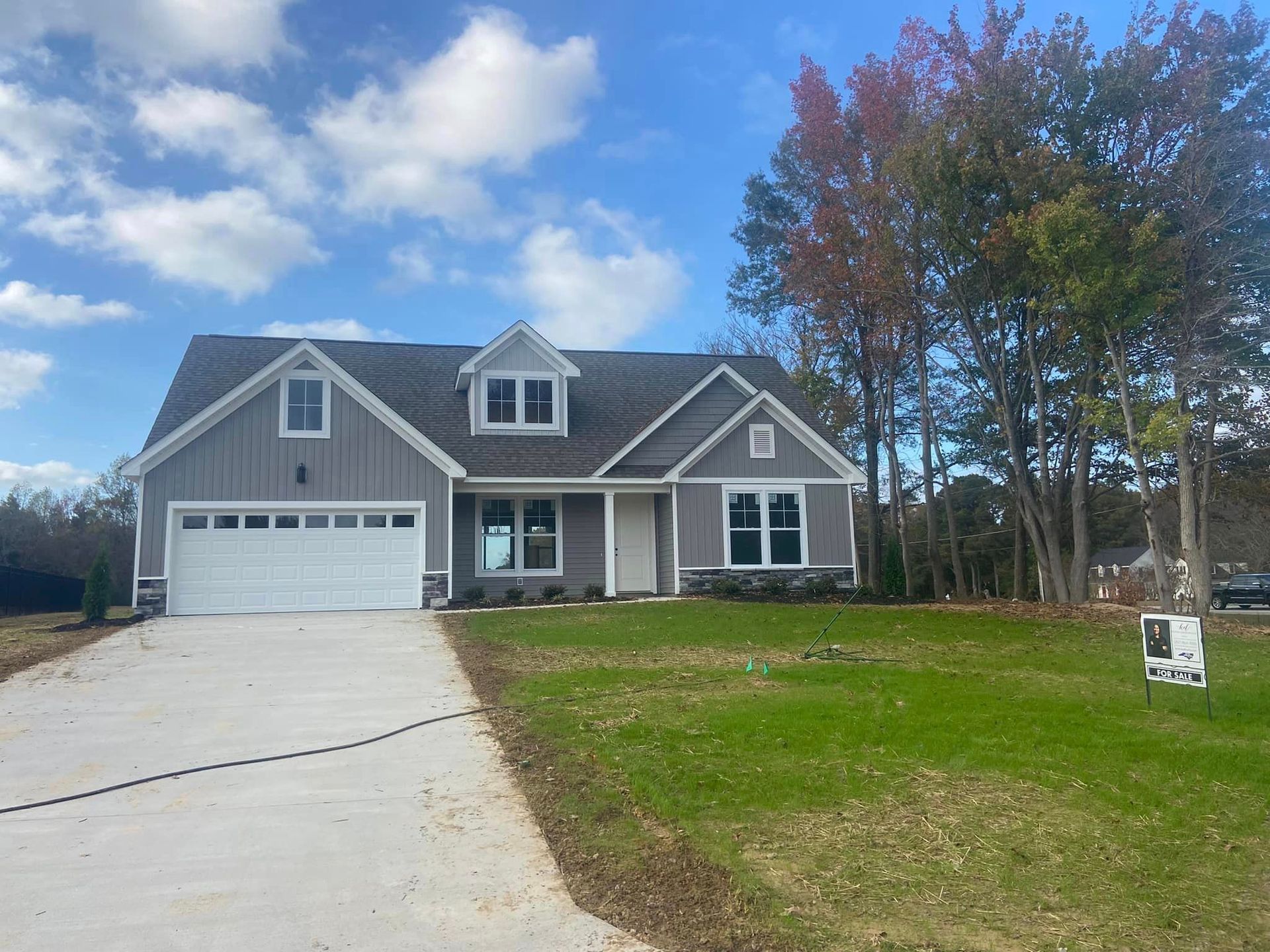 A large gray house with a white garage door is for sale.