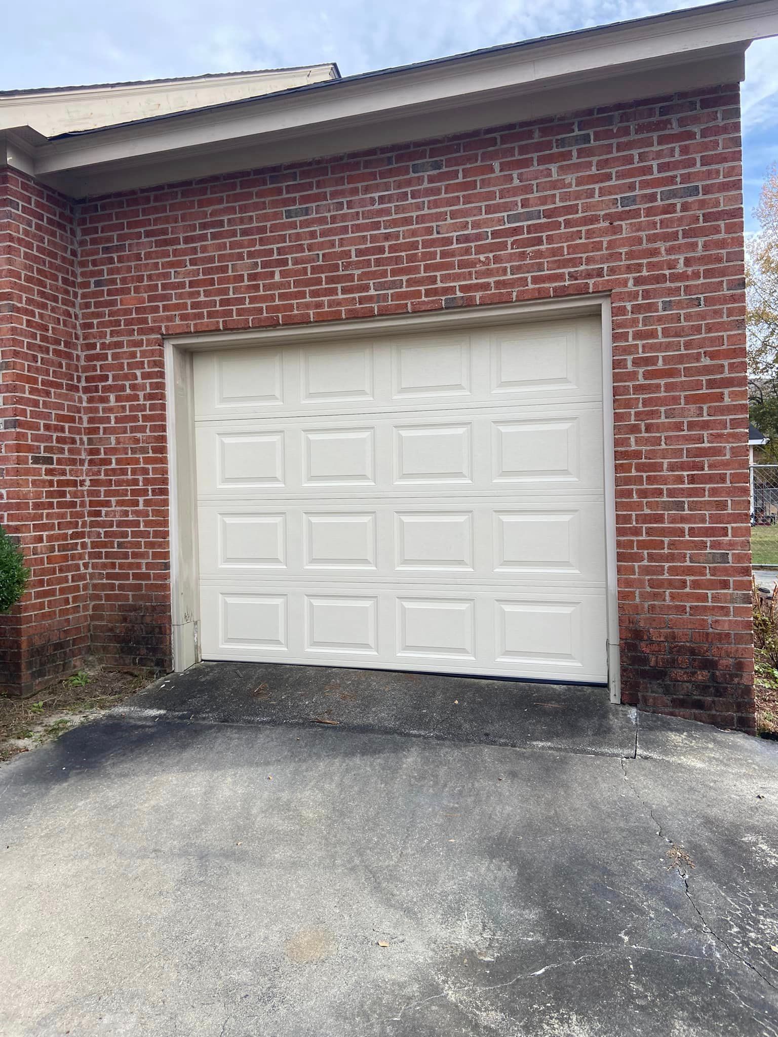 A white garage door is sitting in front of a red brick building.