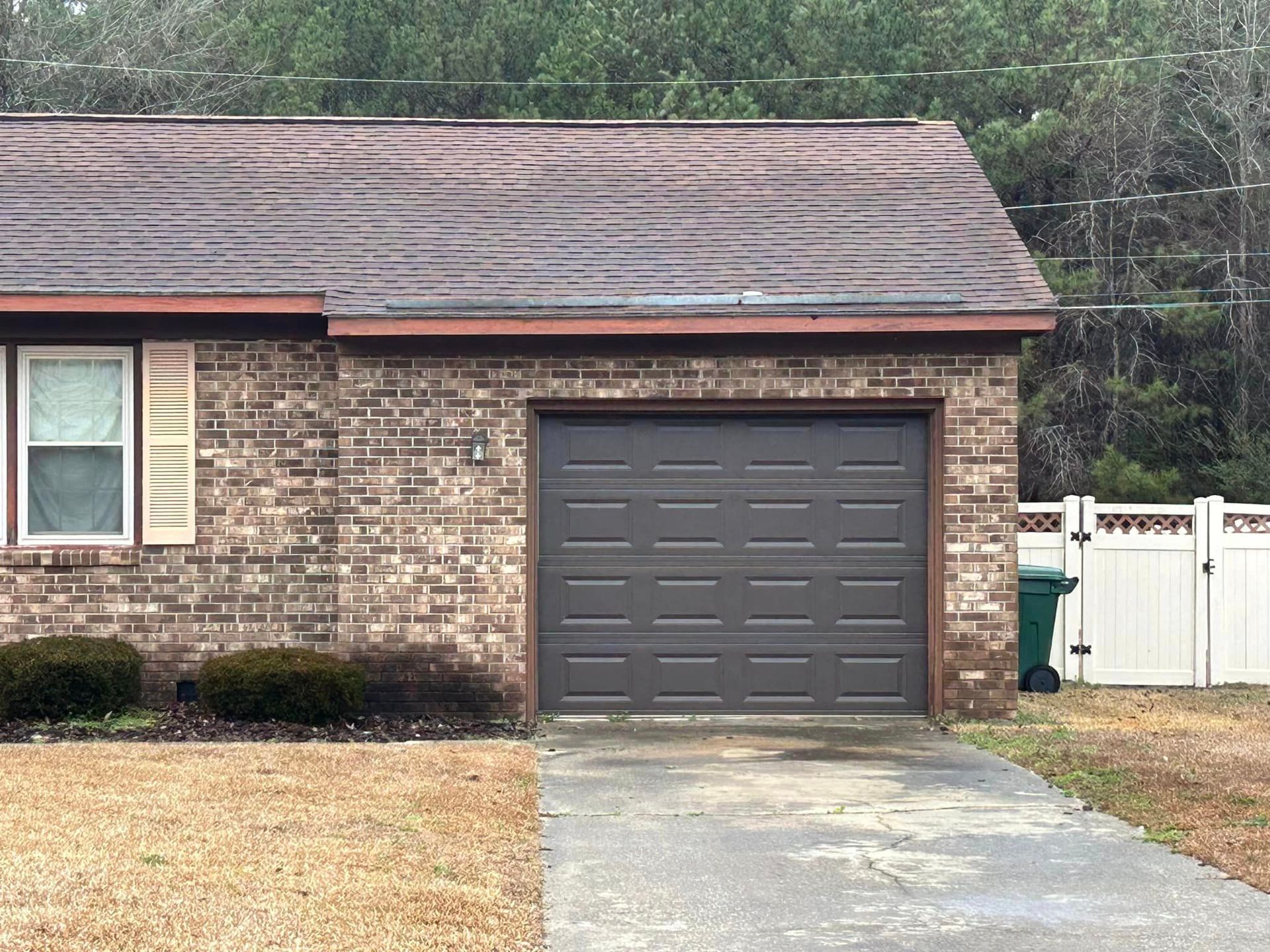 A brick house with a garage door and a white fence.