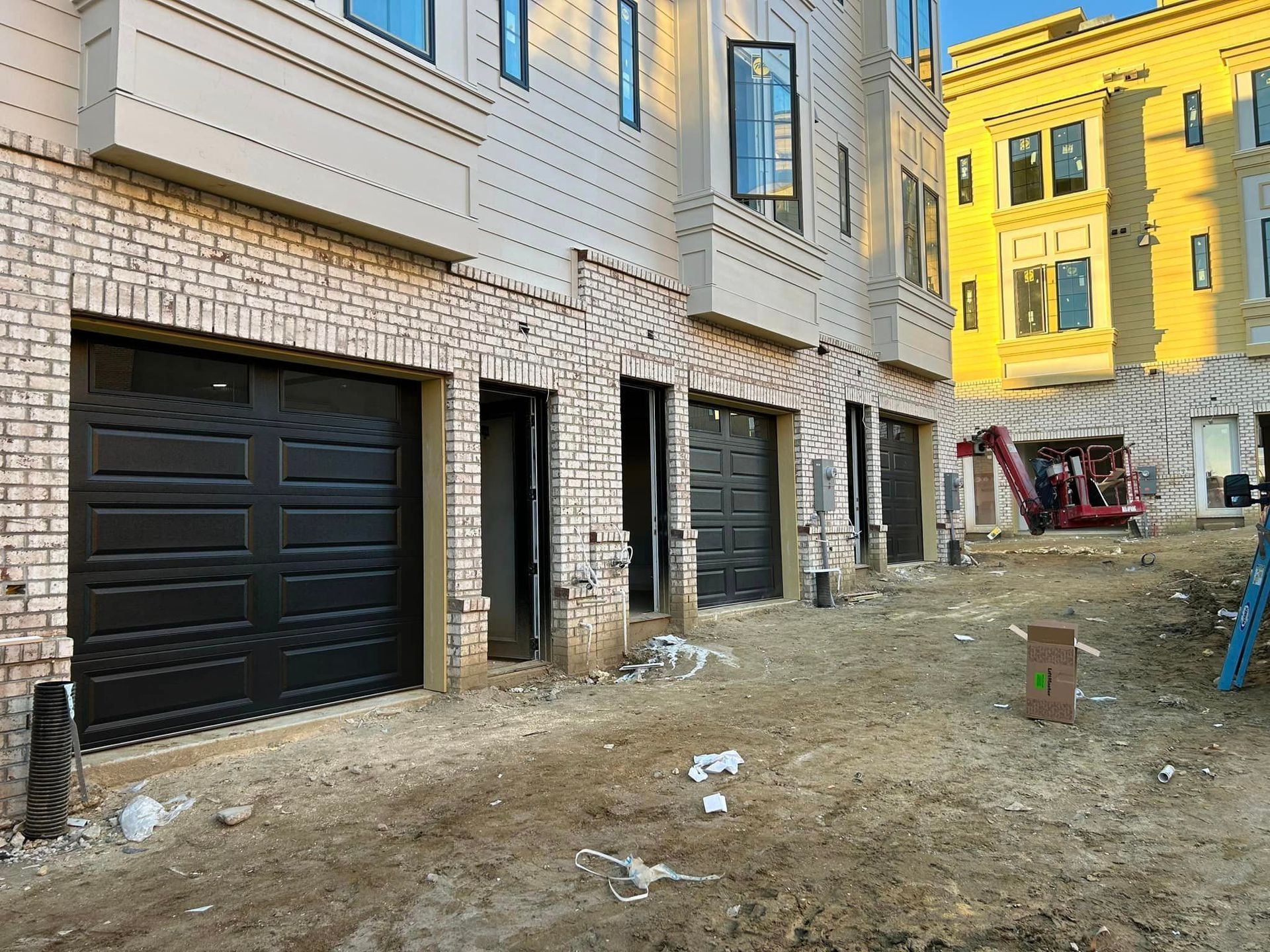 A building under construction with black garage doors and a yellow building in the background.