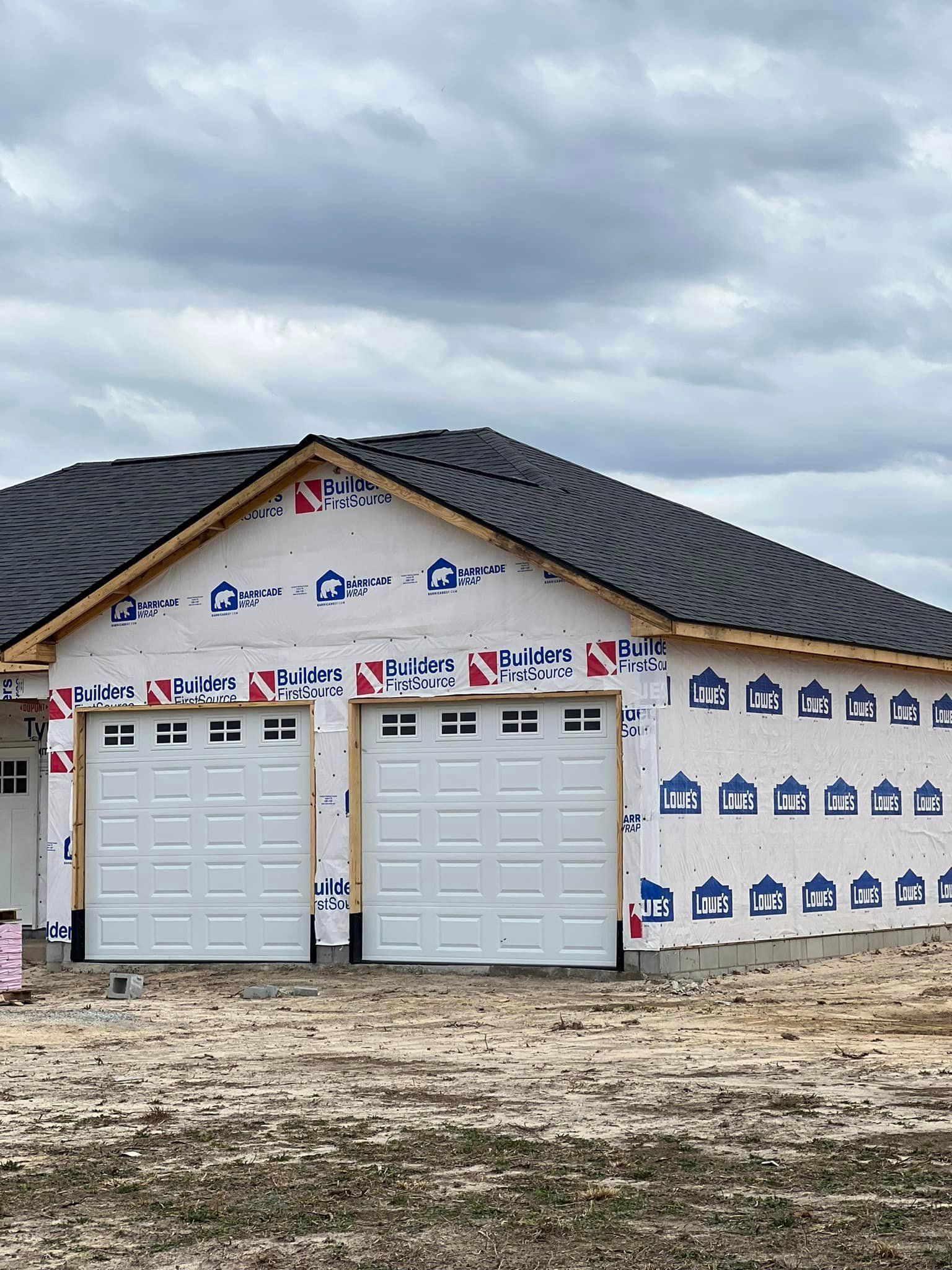 A house is being built with a black roof and white garage doors.