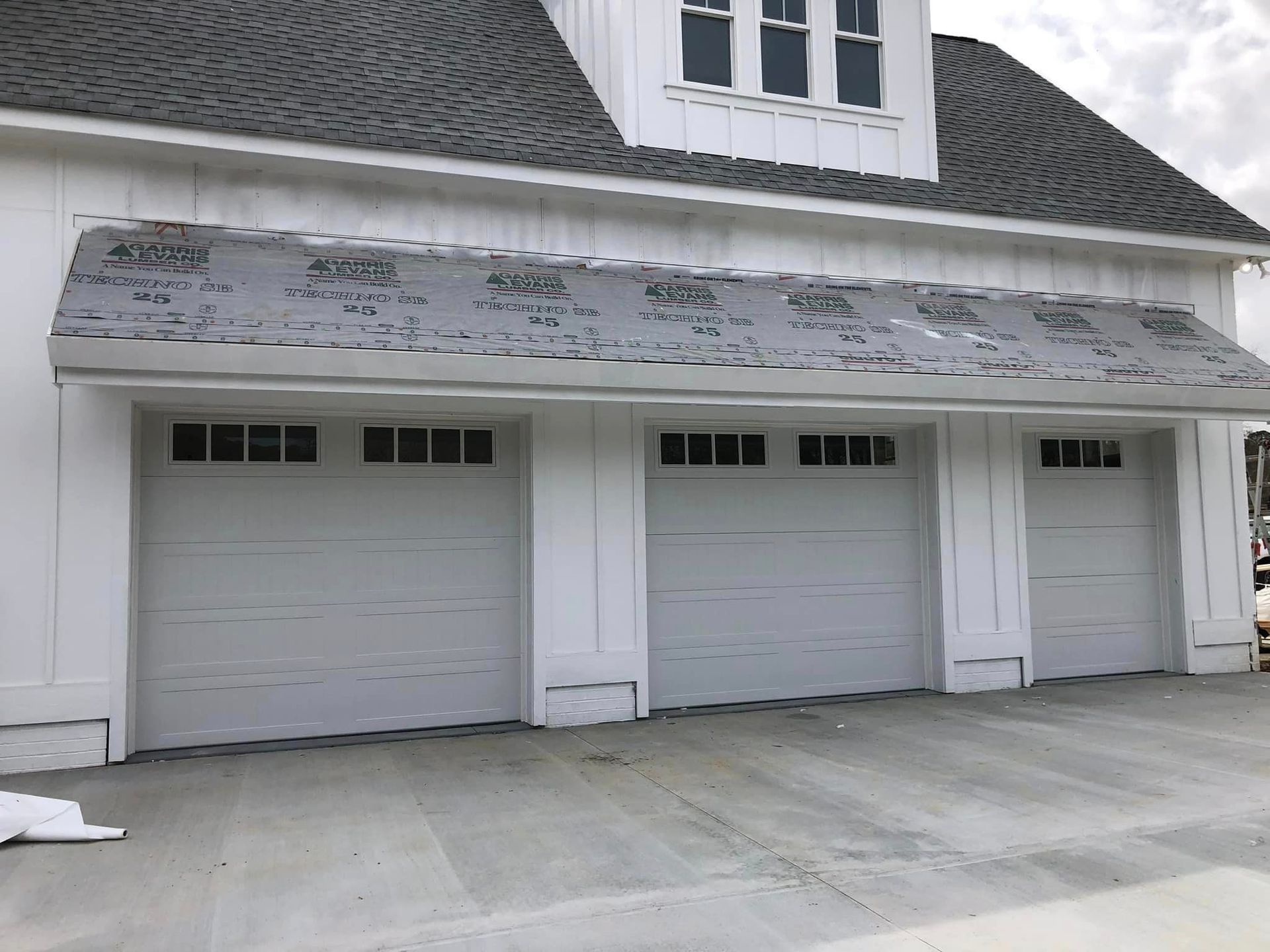 A white house with three garage doors and a gray roof.