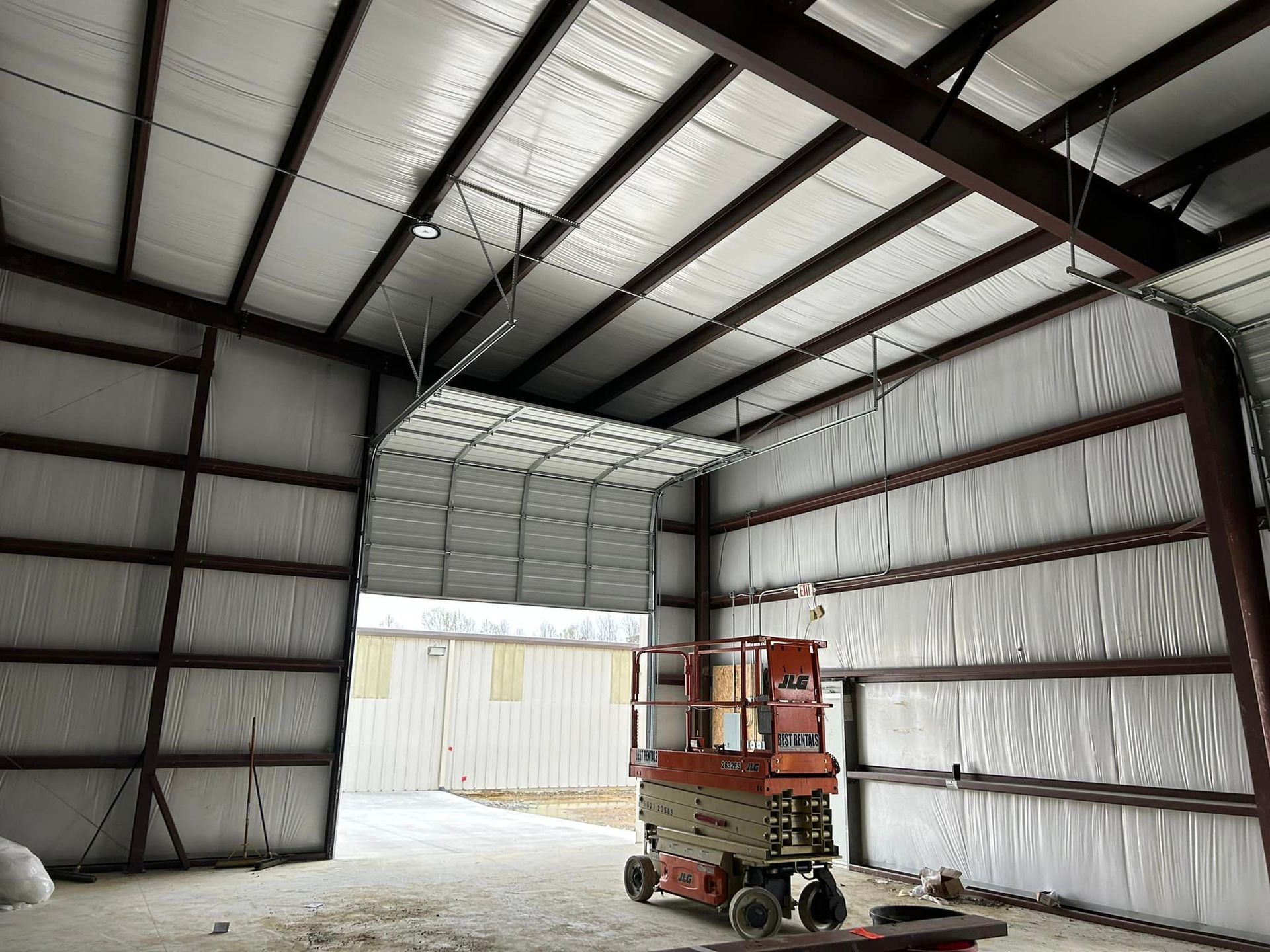 A red scissor lift is sitting inside of a building with a garage door open.