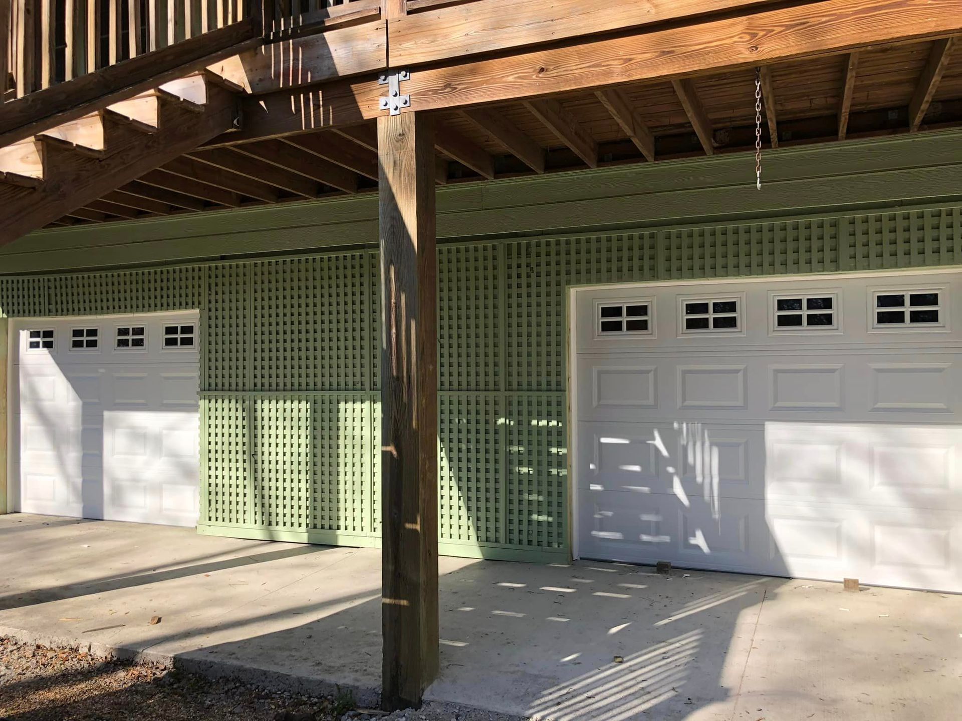 Two white garage doors are under a wooden deck.