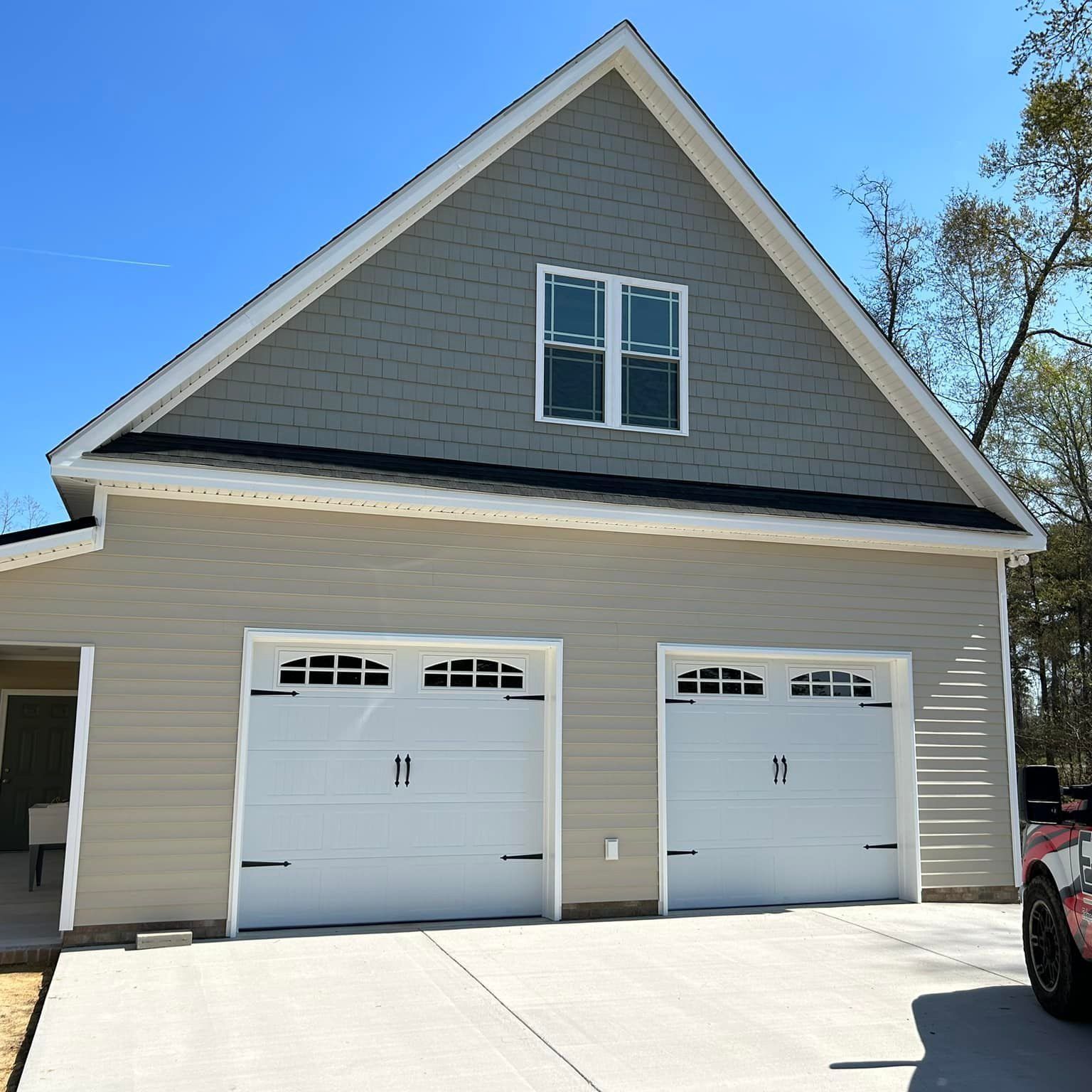 A car is parked in front of a house with two garage doors