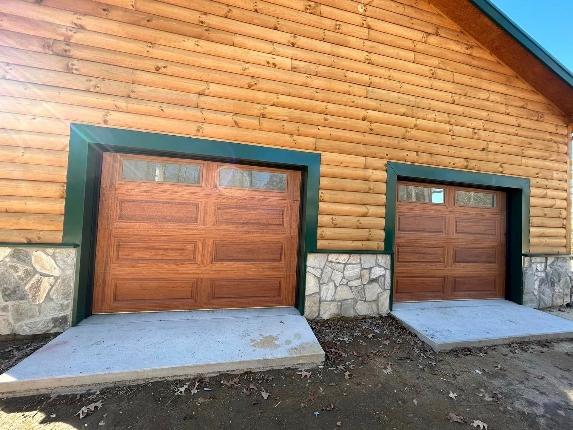 Two wooden garage doors are on the side of a log cabin.