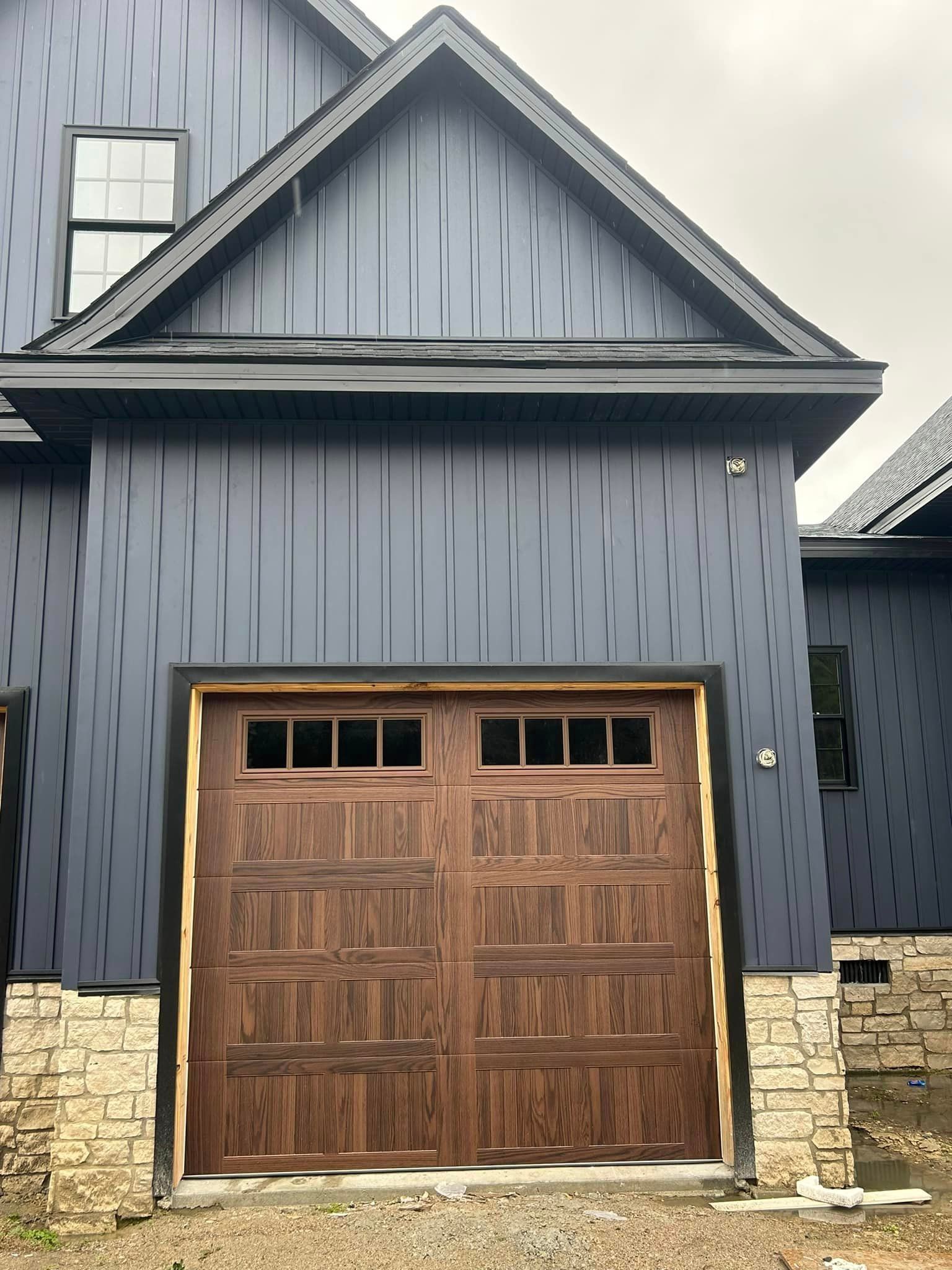 A wooden garage door is sitting in front of a blue house.