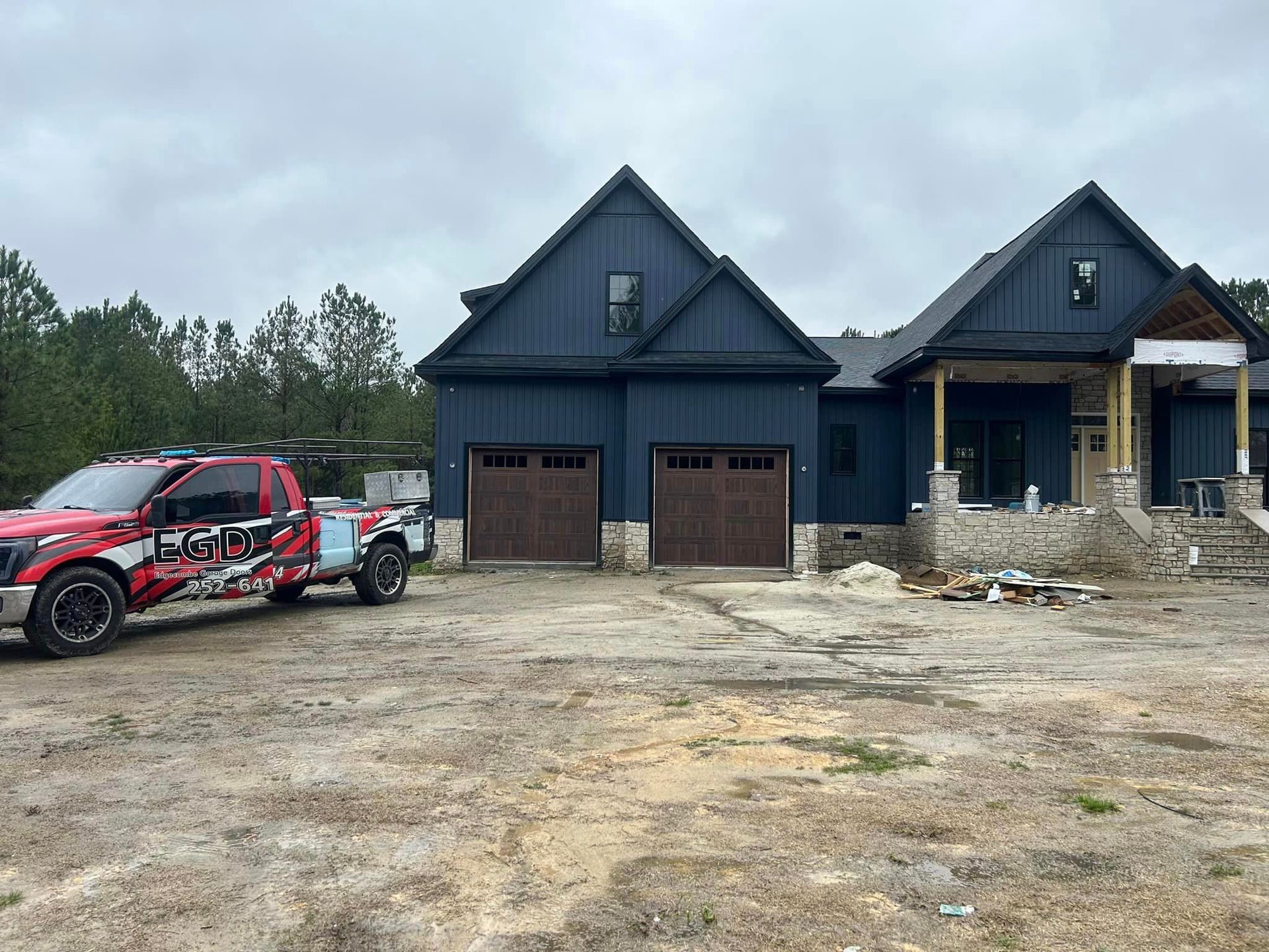 A red truck is parked in front of a large house under construction.