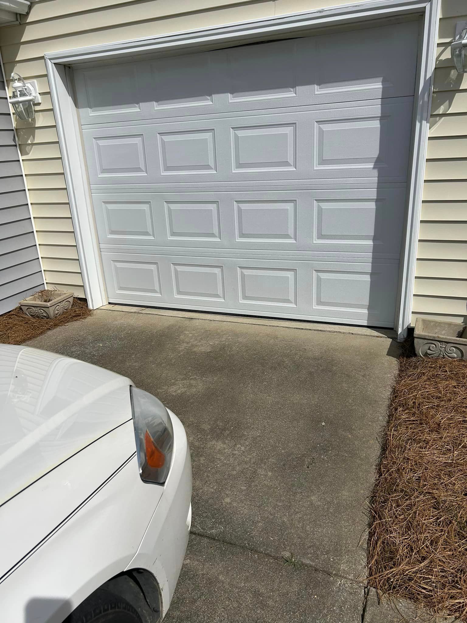 A white car is parked in front of a white garage door.