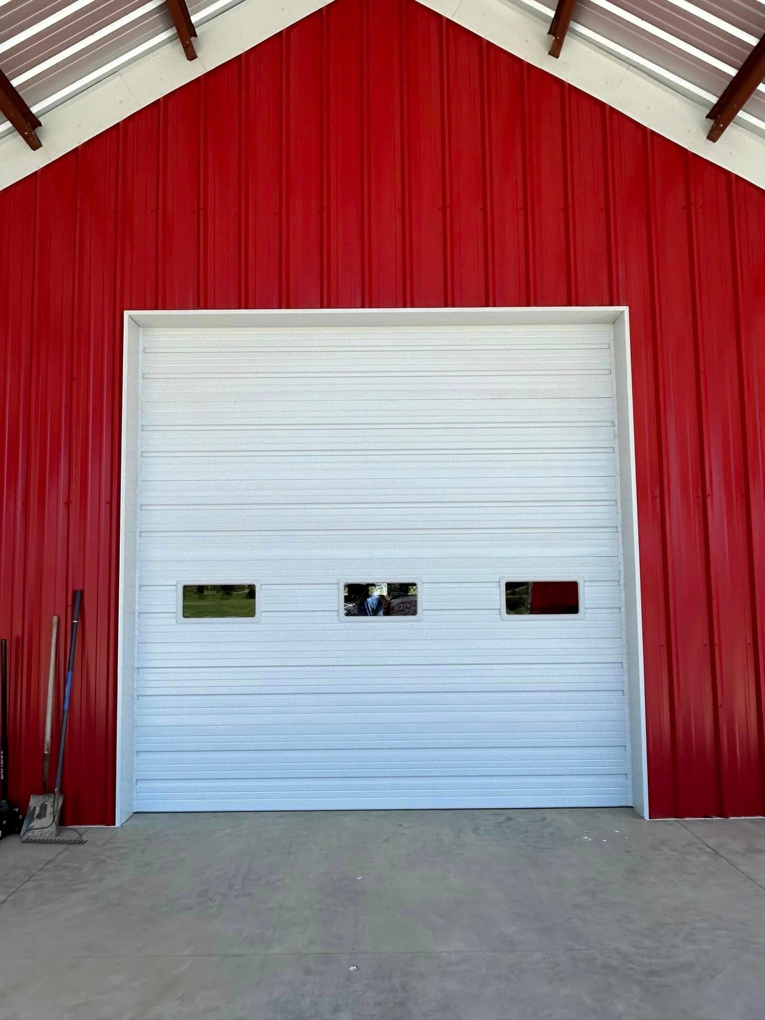 A white garage door is in front of a red barn.