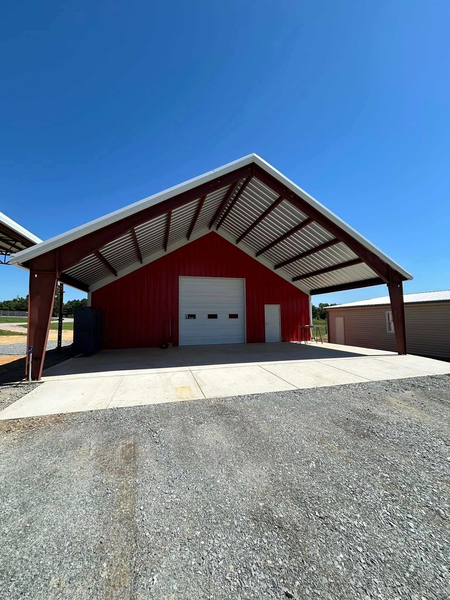 A red barn with a white garage door is sitting on top of a gravel lot.