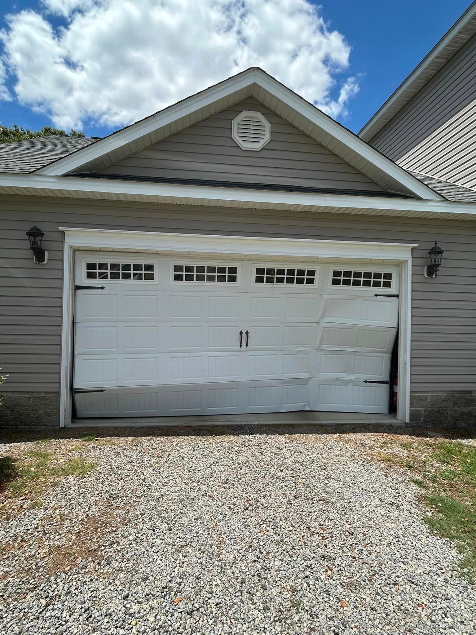A white garage door is open and broken in front of a house.