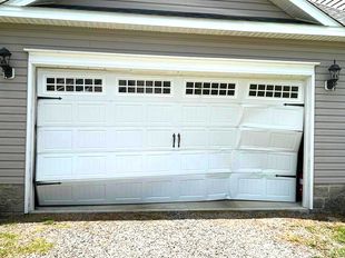 A white garage door is broken in half in front of a house.