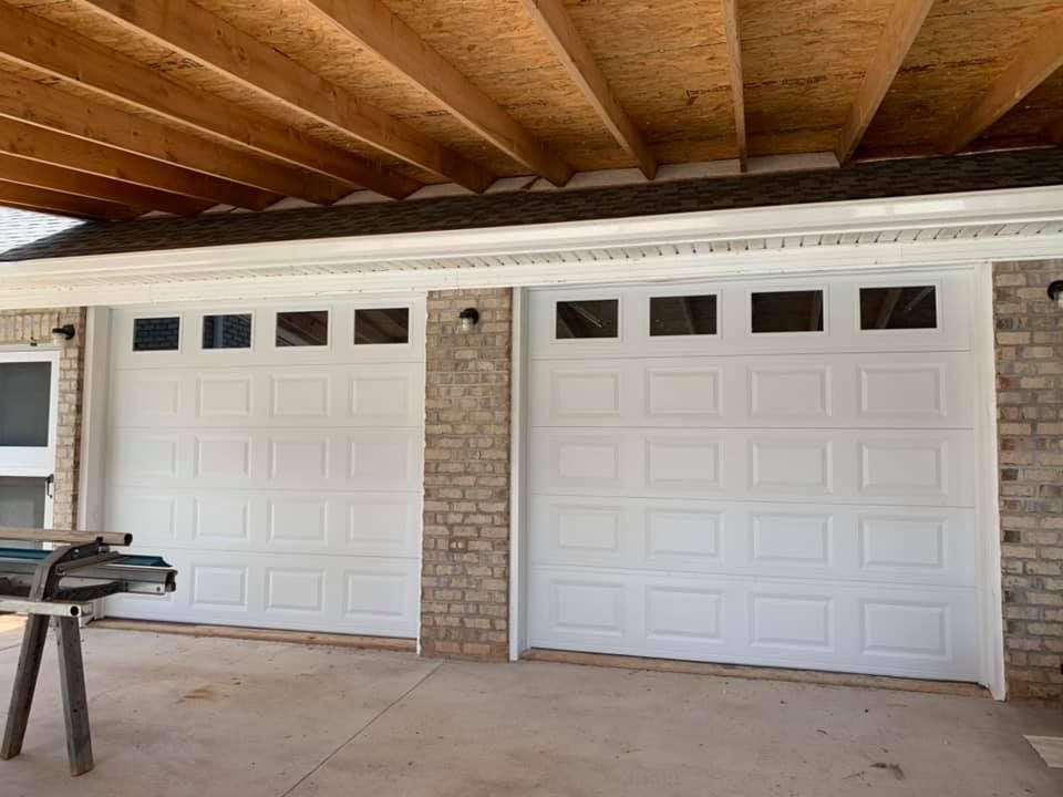 A pair of white garage doors are being installed on a brick house.