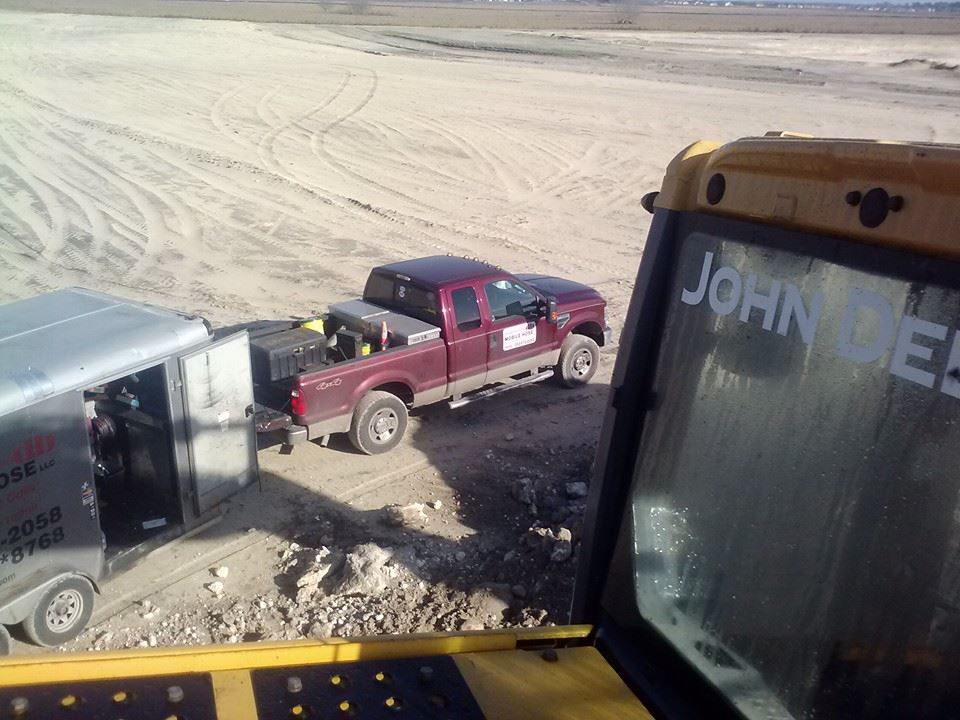 Red pickup truck and trailer parked on a dirt lot, viewed from inside a John Deere vehicle.