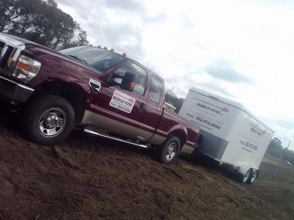 Burgundy pickup truck towing a white trailer on a dirt surface.