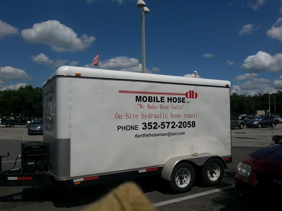 Mobile hose repair trailer, white, parked in a lot on a sunny day, with phone number visible.