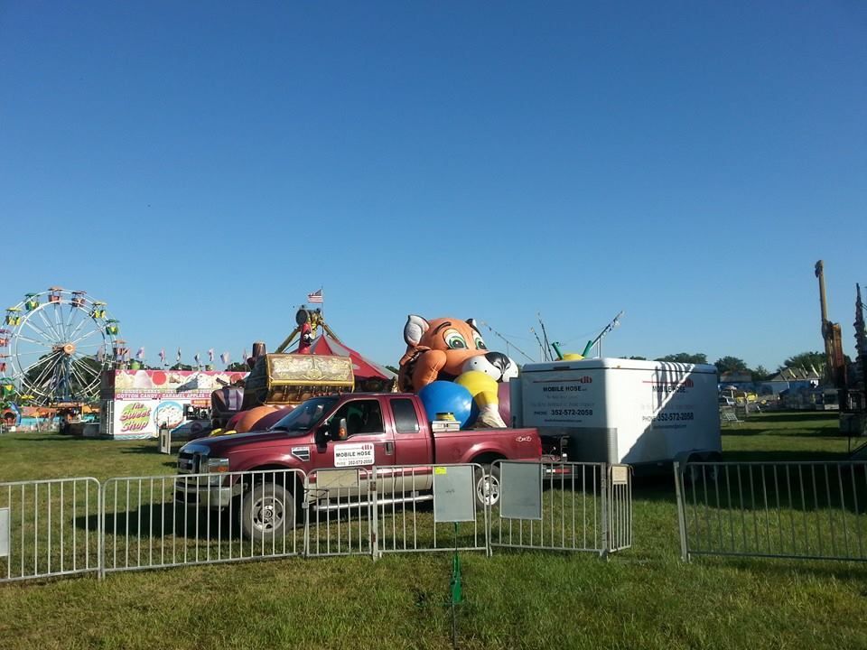A pickup truck with inflatable toys in a field at a fair, Ferris wheel in background, sunny day.