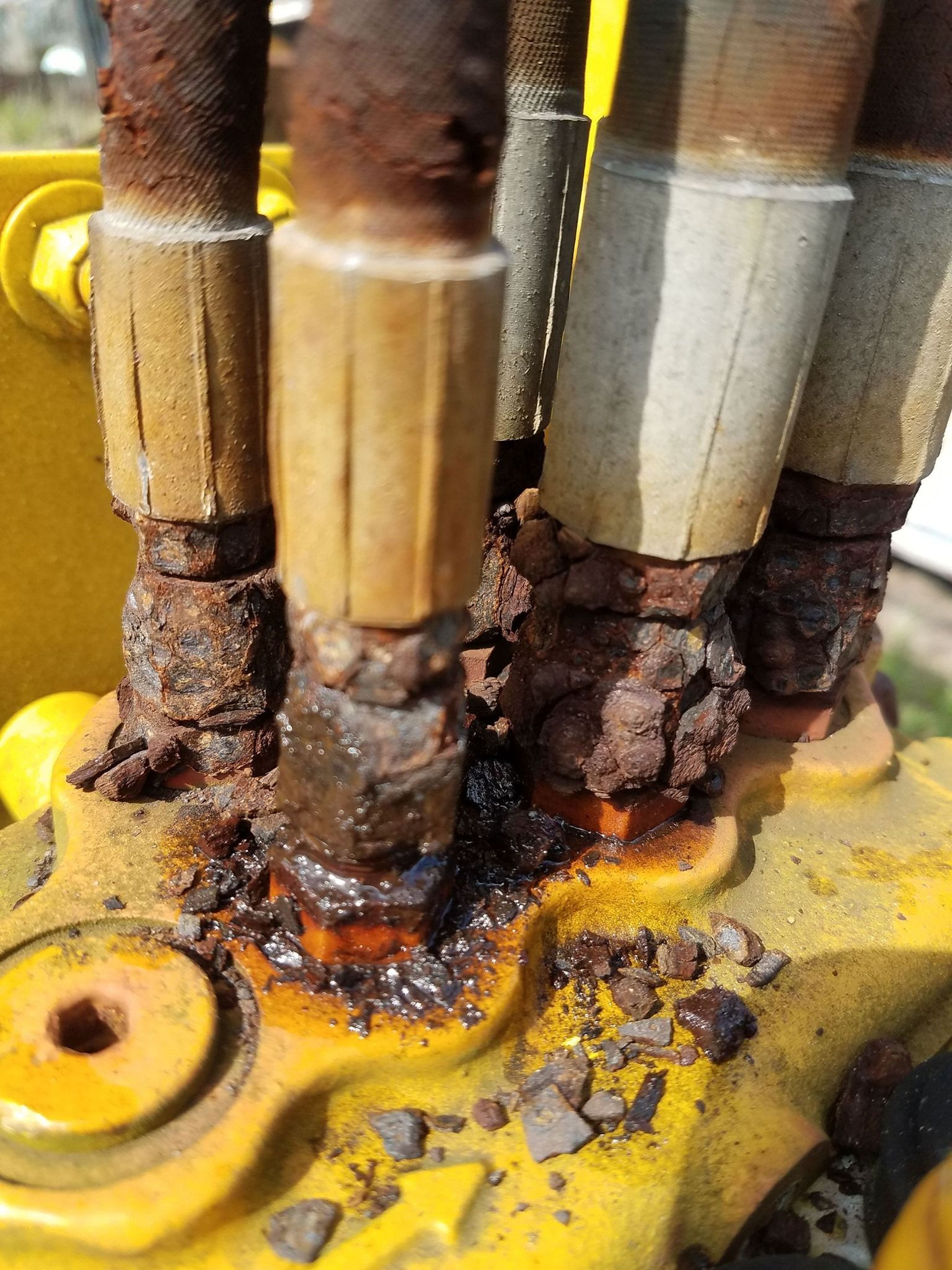 Severely rusted hydraulic hoses connected to a yellow machine; oil leakage is visible.