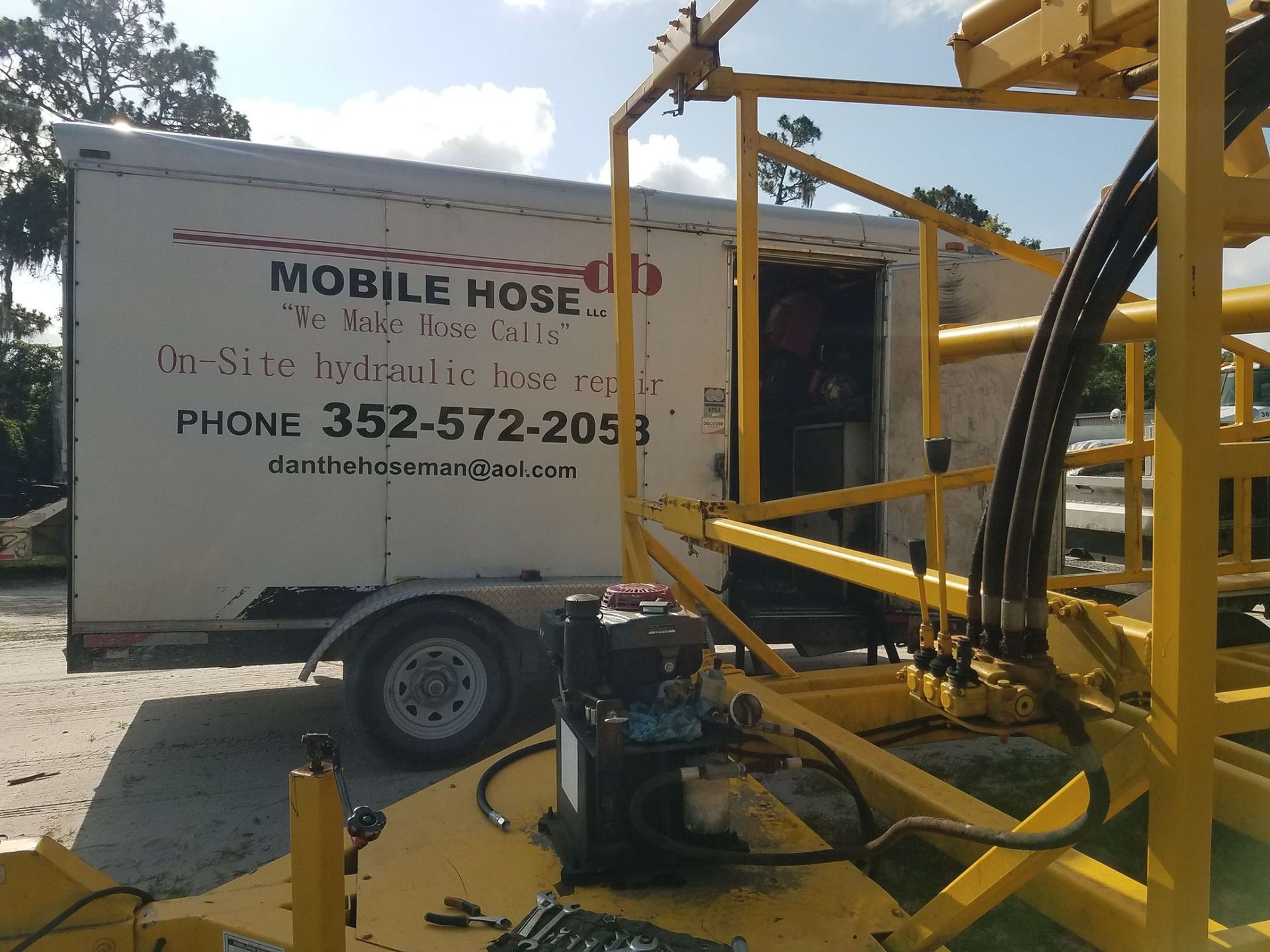 Mobile Hose trailer with yellow machinery nearby, outdoors.