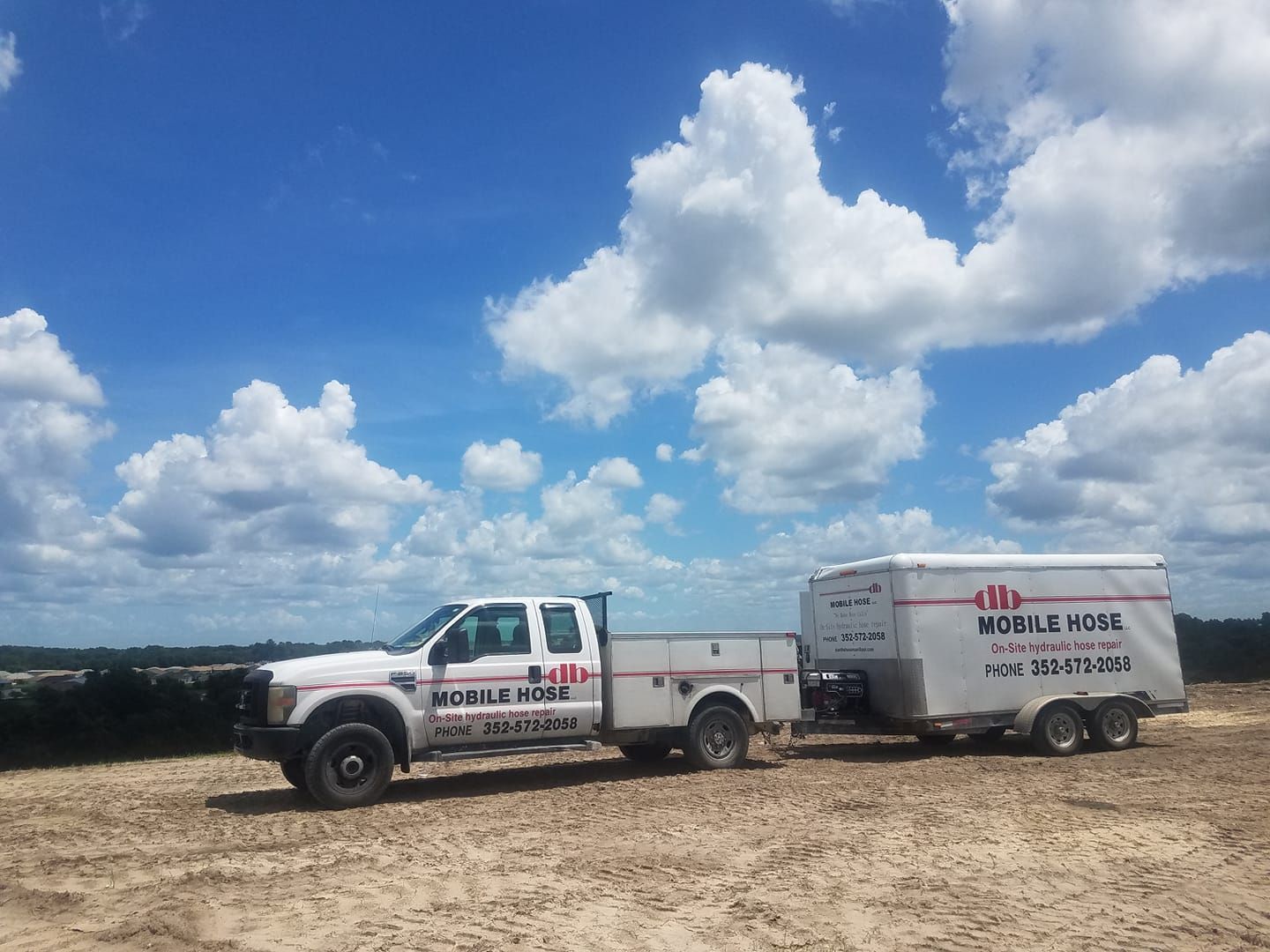 White truck towing a trailer under a blue sky with clouds; 