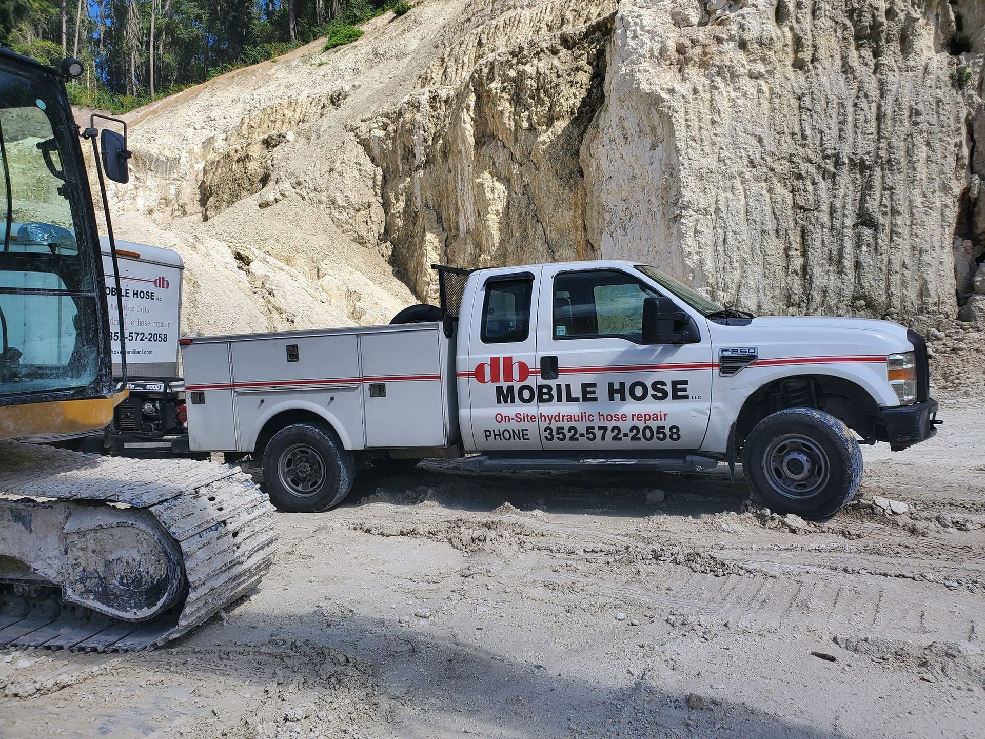 White Mobile Hose truck parked near a rocky cliff and construction equipment.