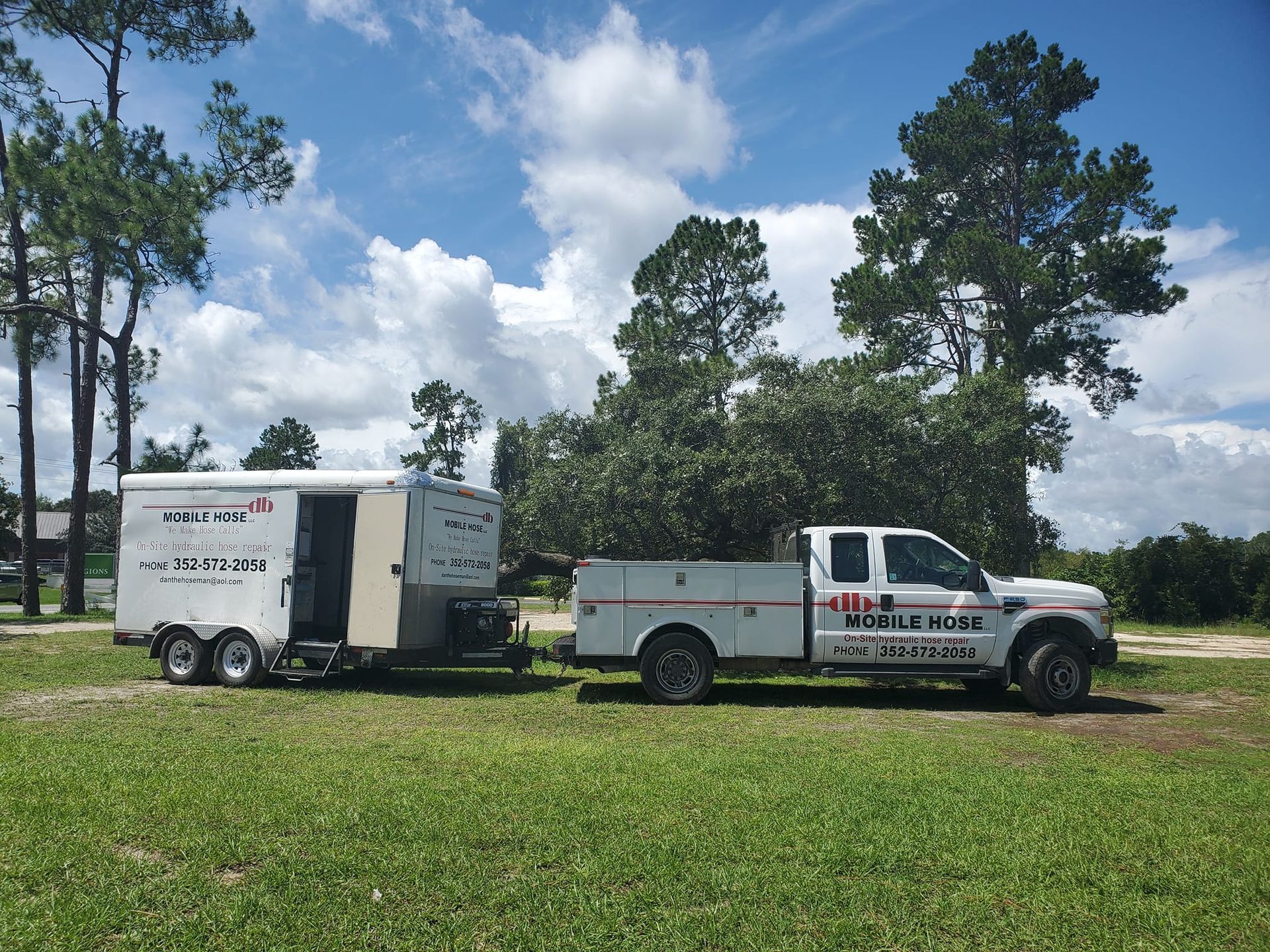 White truck towing a white trailer on grass, under a blue sky with trees.
