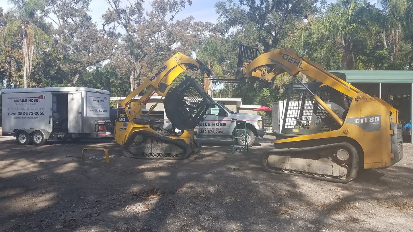 Two yellow construction vehicles working near a trailer and a building.