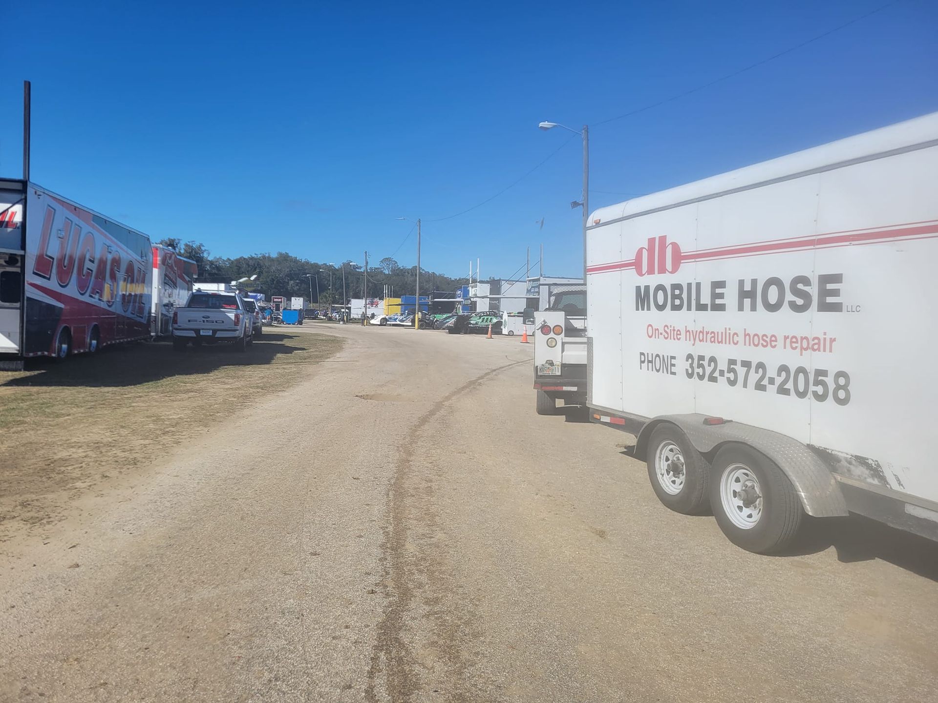 A dusty road lined with trailers and vehicles on a sunny day. A Mobile Hose trailer is in the foreground.