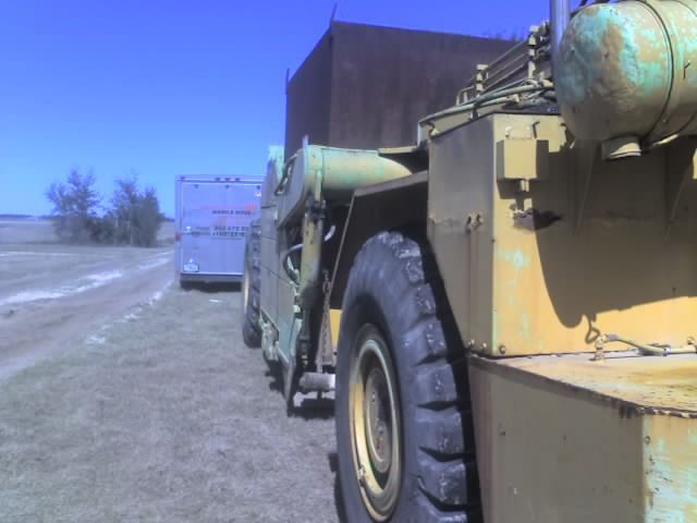 Yellow industrial vehicle on a dirt road, facing a white vehicle under a clear blue sky.