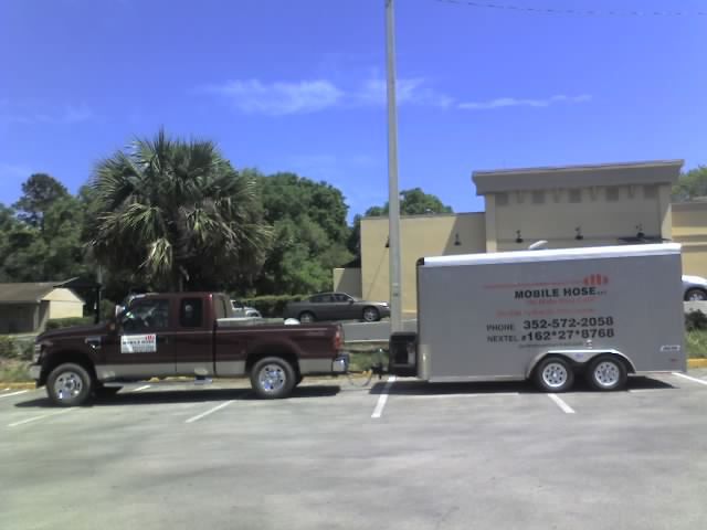 Brown truck with trailer parked in a lot. Trailer has business name and phone number. Sunny day.