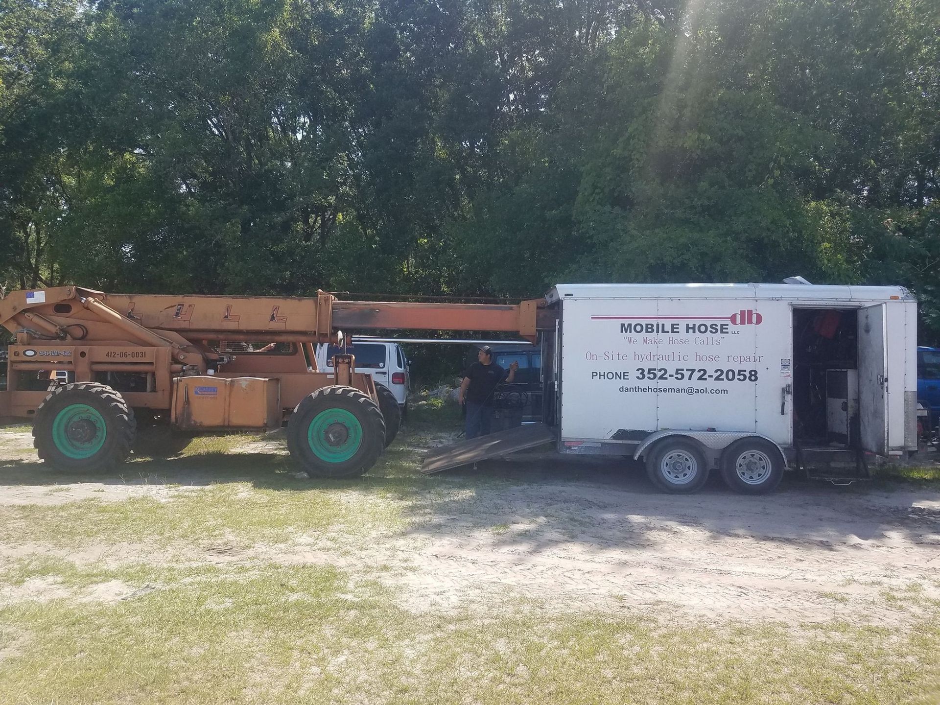 A large orange forklift next to a white trailer with 